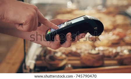 Close-up of woman making payment through NFC in bakery, cafe restaurant, mobile phone contactless pay for bill with terminal, banking