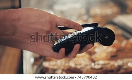 Close-up of woman making payment through NFC in bakery, cafe restaurant, mobile phone contactless pay for bill with terminal, banking