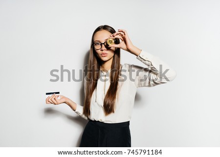 a young successful girl in a white shirt and glasses is holding a golden bikoin and a bank card