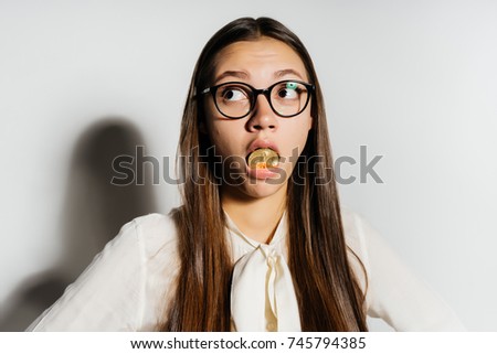 a funny modern girl with glasses is holding a gold bitcoin in her mouth