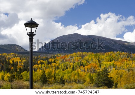 The mountainsides in Summit County, Colorado shimmer with the orange, gold and green colors of autumn.  Pictured here is a Victorian lamp post with Buffalo Mountain in the background.