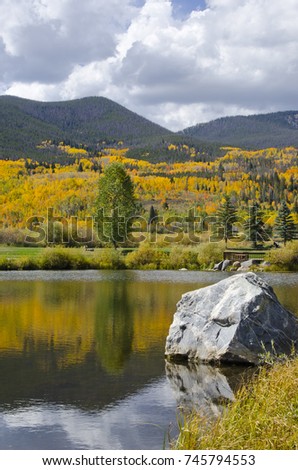 The mountainsides in Summit County, Colorado shimmer with the orange, gold and green colors of autumn.  Pictured here are the pine and aspen forests cascading down the mountains, with a lake.