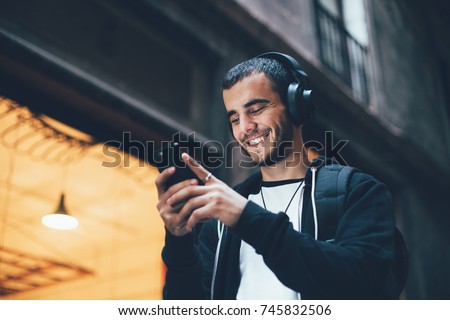 Cool trendy young millennial from generation z laughs and smiles on camera, walks outside with smartphone and big wireless headphones, enjoys new technology and immersive reality Royalty-Free Stock Photo #745832506