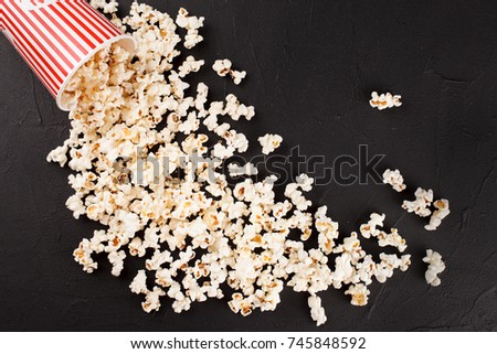 Popcorn banner - red stripped paper cup and kernels lying on dark background for cinema card or flyer.