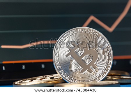 Coins of bitcoins lie on the table in front of and next to the tablet on which charts of Bitcoin's cost growth are visible. The concept of crypto currency
