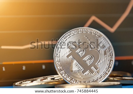 Coins of bitcoins lie on the table in front of and next to the tablet on which charts of Bitcoin's cost growth are visible. The concept of crypto currency