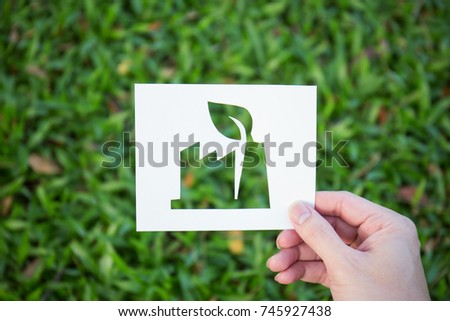 Hands holding cut paper with the logo of factory shape over green glass background. friendly green living. Sign and symbol background banner template of environment friendly concept. Earth day