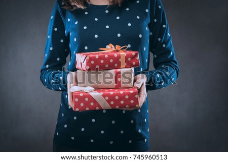 Close up cropped shot of a girl dressed in dotted sweater holding batch of gift boxes wrapped in craft paper and decorated with satin ribbon in her hands.