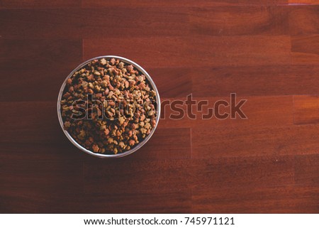 Dry animal food in stainless bowl on  parquet wood floor, Top view.