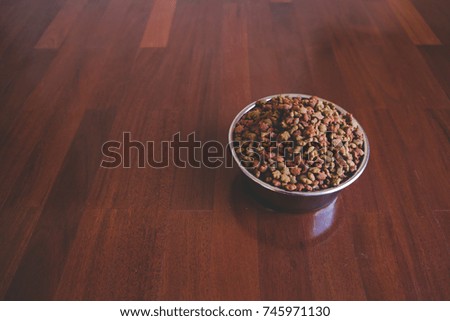 Dry animal food in stainless bowl on  parquet wood floor.