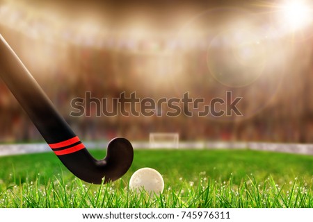 Low angle view of field hockey stick and ball on grass and deliberate shallow depth of field on brightly lit stadium background with lens flare and copy space.