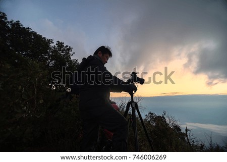 photographer silhouette with accessories and holding hand on tripod , taking pictures of the beautiful moments during the sunset ,sunrise

