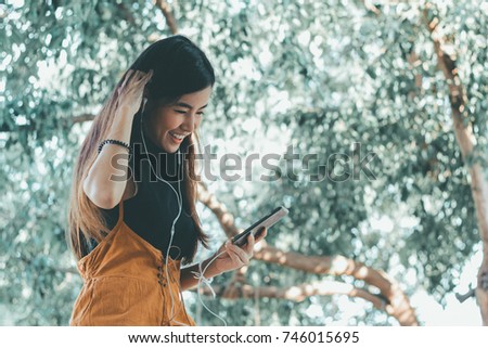 Young asian Student woman wearing earphones, listening to the music with nature background - Retro Vintage Film look effect 
