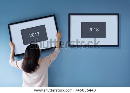 Rear view Asian woman holding and putting picture frame on the blue wall. Female decorating room. Moving and renovate house. 2017, 2018, 2020, 2021, Start and change to New Year concept