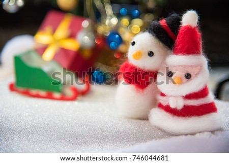 Santa claus and snowman wool doll on snow set up with xmas tree, red gift box, sled, bokeh decorations light christmas background