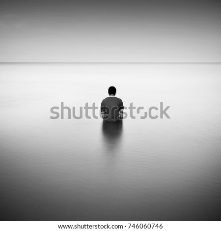 Fine art black & white image of one man standing in the sea. Soft Focus due to long exposure