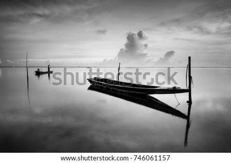 Black & white scenery of traditional fishing boat at Tumpat, Malaysia with fisherman silhouette standing on the boat. Soft focus due to long exposure.   Royalty-Free Stock Photo #746061157