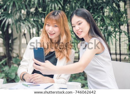 Two pretty young woman taking selfie from hand with smart phone and smiling in the garden, Urban life concept.