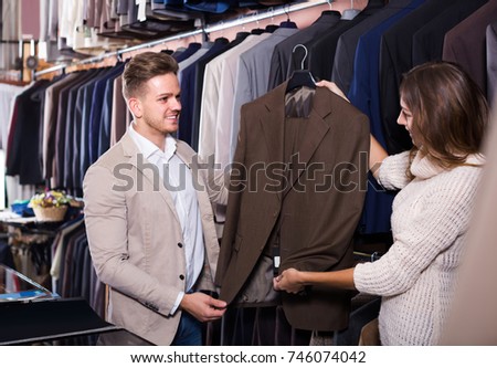 Young spanish couple choosing new suit in men`s cloths store