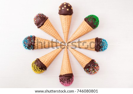 Chocolate cake pops in waffle cone for ice cream in assortment, located in a circle, decorated with confectionery sprinkles on white wood table. Picture for a menu and confectionery catalog. Top view.