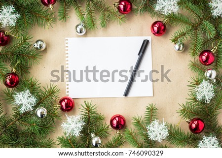 Festive christmas border with red and silver balls on fir branches and snowflakes on rustic beige background with copyspace and pen.