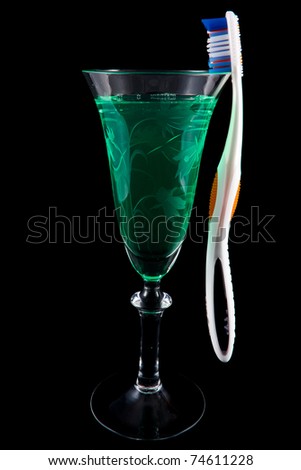 Picture of moutwash in a wine glass with a tooth brush hanging on the side