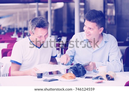 Couple of male tourists with map talking and drinking coffee