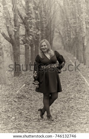 Black&white portrait of a beautiful plus size blonde girl in a black dress outdoor in the autumn park. She standing on the alley full of yellow leaves.