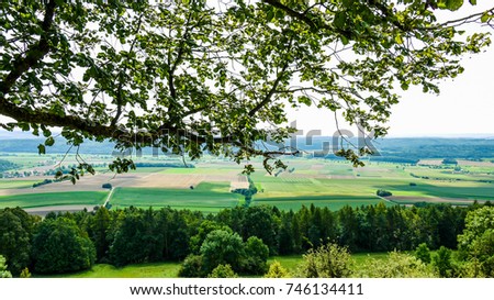 View from the top of the Hesselberg mountain in Bavaria, Germany on a sunny summer day. Showing the surrounding landscape through the leaves of a tree.