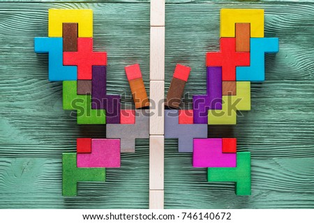 Colorful wooden puzzle in butterfly shape on green wooden background. Abstract butterfly, two halves of a whole, mirror reflection.