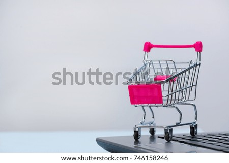 Shopping cart or supermarket trolley with laptop notebook on grey background and copy space, e-commerce and online shopping concept.