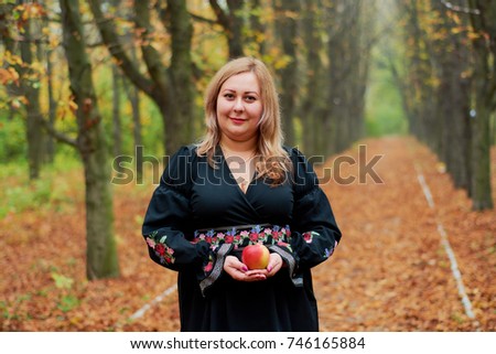 Portrait of a beautiful plus size blonde girl in a black dress with a big shawl on her shoulders. She standing against the background of a wall of multi-colored leaves in the autumn park.