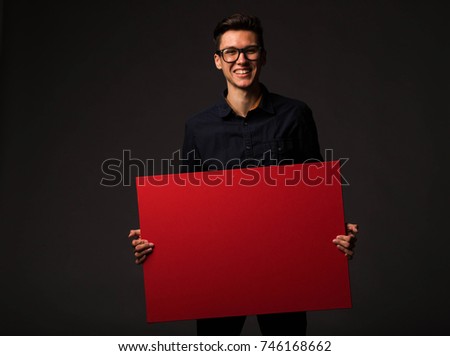 Young happy man portrait of a confident businessman showing presentation, pointing paper placard black background. Ideal for banners, registration forms, presentation, landings, presenting concept.