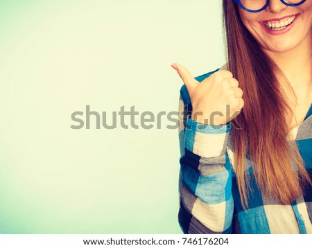 Happiness and fun concept. Happy smiling woman in checked shirt showing ok, good, thumb up gesture. Studio shot on blue background