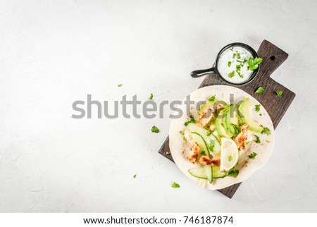 Healthy food snack. Tortillas taco with grilled chicken, avocado, fresh salsa, lettuce, lime. With yogurt & parsley sauce. On light gray stone marble table, wooden cutting board. Top view copy space