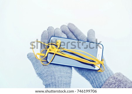 Female hands in gloves hold mobile phone with the yellow headphones connected.