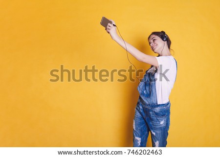 A teenage girl in headphones makes a selfie on a bright orange and yellow background. Place for your text.