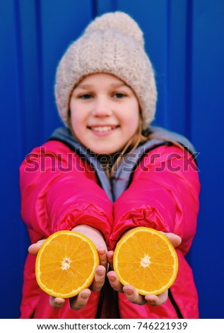 Happy little girl with oranges on a blue background out of doors.