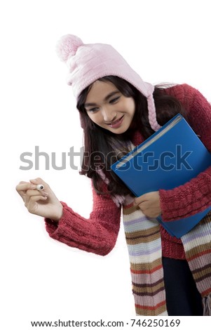 Photo of female college student wearing winter clothes while writing on the whiteboard and holding a folder 