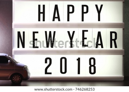 Pieces of english text spelling new year 2018 on illuminated lightbox in the scene appear miniature plastic car model as a blurry foreground.