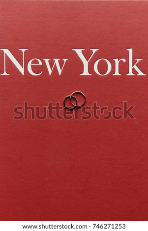 Wedding rings lie on red book with lettering 'New York'