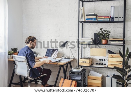 Handsome young Caucasian businessman sitting at  office and reading from papers. Royalty-Free Stock Photo #746326987