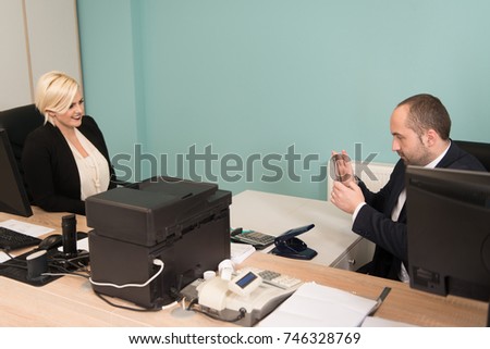 Young Cheerful Business Man Working With Computer at Desk in the Modern Office and Taking Pictures From Coworker With Mobile Phone