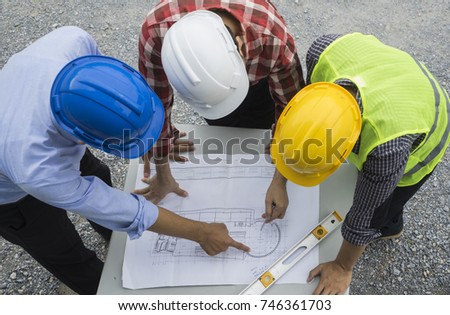 Top view Civil engineer wearing safety helmet and green reflective vest working on site, discussing on details of blue print on table with water staff gauge, Real estate construction  business concept Royalty-Free Stock Photo #746361703