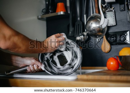 washing dishes. male hands in foam washes the frying pan with a detergent and sponge in the kitchen of the house. Royalty-Free Stock Photo #746370664