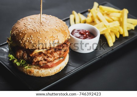 Juicy burger with french fries and ketchup on the black background. Toned
