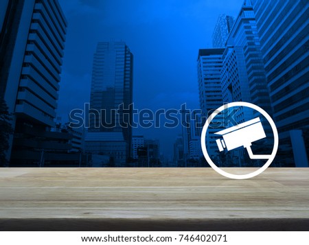 cctv camera icon on wooden table over modern office city tower background, Business security concept