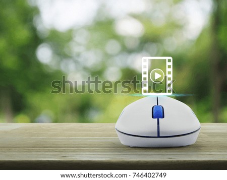Play button and movie icon with wireless computer mouse on wooden table over blur green tree in park, Cinema online concept