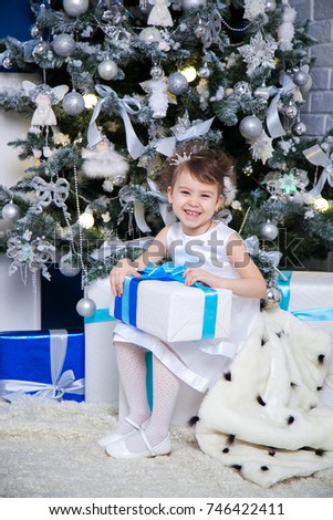 Little girl opening christmas present in front of the fir tree 