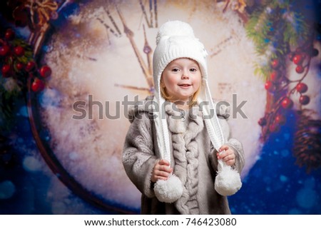 Little girl in winter hat and fur coat against the background of New Year's clock
